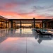 Large modern polished concrete patio with infinity pool and industrial chic architecture at sunset.