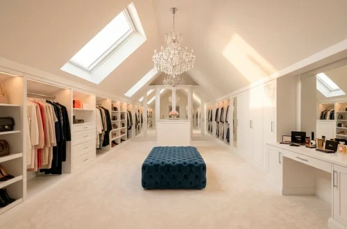 Luxurious boutique-style attic wardrobe with white custom cabinets, sloped ceilings, and a crystal chandelier.