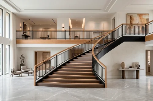 Modern luxury staircase with oak and black metal railing in a bright sunlit foyer.
