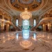 Grand tiered crystal chandelier hanging in a luxury marble foyer with a sweeping grand staircase.