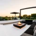 Wide landscape of a modern minimalist black and white patio with a fire pit and sleek furniture.