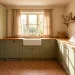 Wide landscape view of a cozy cottage laundry room with sage cabinets, farmhouse sink, and sunlight.