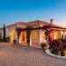 Luxurious Mediterranean villa exterior with white stucco walls, terracotta roof, and blooming bougainvillea at sunset.