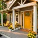 Wide view of a sunny front porch with a mustard yellow door and lemon Adirondack chairs at sunset.