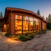 Luxurious modern log cabin with huge glass walls and traditional wood siding at twilight.