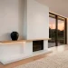 Wide 2:1 banner of a modern minimalist fireplace with a white plaster finish and a single black ceramic vessel.