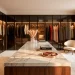 Wide view of a luxury minimalist dressing room with marble island and glass wardrobes.