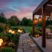 A peaceful backyard at twilight featuring glowing orb floor lights and hanging Moroccan lanterns on a pergola.