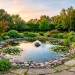 A serene backyard featuring a small DIY garden pond with a solar fountain at sunset.