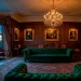 Grand Victorian parlor with emerald velvet sofa and luxurious plum chaise longue in warm light.