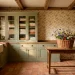 A wide view of a cozy cottage laundry room with sage green cabinets and floral wallpaper.