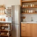 Wide view of a modern studio apartment kitchen with organized pantry shelves, glass jars, and a rolling storage cart.