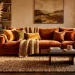 Cozy autumn living room with layered velvet pillows, knit blankets, and dried grass in warm natural light.