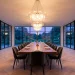 Luxurious modern dining room with walnut table, velvet chairs, and a large glass chandelier at sunset.