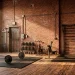 A stylish urban loft gym featuring an exposed red brick wall, black fitness equipment, and large factory windows.