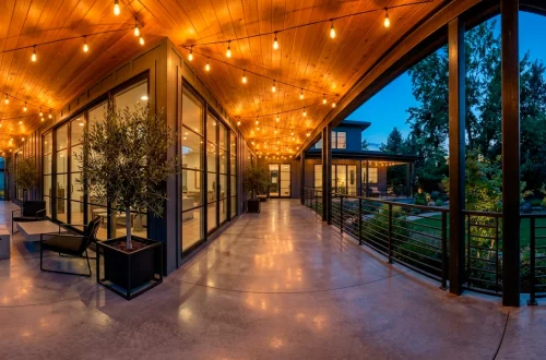 Modern industrial wrap-around porch featuring a smooth concrete floor, black steel railings, and warm cedar ceiling.