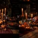 Moody dark cottagecore Thanksgiving dining table featuring glowing taper candles, dark linen, and tarnished silver.