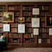 Wide landscape shot of a luxury home library with integrated gallery wall and cozy reading chair in warm lighting.