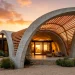 Modern home exterior featuring a bold sculptural porch with sweeping concrete arches and geometric wood louvers at sunset.