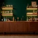 Modern small home bar in an alcove with walnut cabinets and brass cocktail tools against an emerald green wall