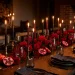 Sophisticated moody Valentine's Day tablescape with dark red roses and flickering taper candles.