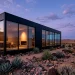 Cinematic 2:1 wide shot of a modern minimalist black villa at twilight with glass reflections.