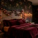 Dimly lit romantic cottagecore bedroom with dark floral wallpaper, vintage brass candelabras, and burgundy velvet bedding.