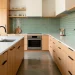 Modern upscale kitchen featuring a glossy sage green tile backsplash and minimalist light oak cabinets.