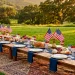 A luxurious patriotic picnic setup with navy linens and vintage flags on a green lawn at sunset.
