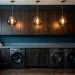 Moody dark laundry room featuring three glowing brass and smoked glass pendant lights over a slate counter.