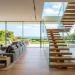 Wide view of a modern open-plan living room featuring a minimalist floating glass staircase and white oak floors.
