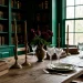 Wide banner of a moody dark academia dining room decorated with antique books and brass candlesticks for Mother's Day.