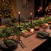 A modern holiday dining table featuring matte black accents, dark stoneware, and elegant greenery under warm lighting.