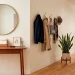 A modern and organized apartment entryway featuring a slim console table, wall hooks, and a round mirror.