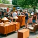 Shoppers browsing authentic Mid-Century Modern and Art Deco antiques at a sunny outdoor flea market.