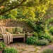 Wide view of a rustic stone garden reading nook with a plush wooden bench and green cushions under an oak tree.