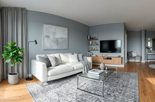 Wide view of a modern small living room decorated in cool-tone greys with a white sofa and sheer curtains