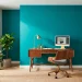 Modern home office featuring a vibrant teal accent wall, mid-century wood desk, and lush green plants.