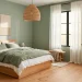 Serene minimalist bedroom featuring soft sage green walls, warm oak furniture, and crisp linen bedding