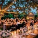Romantic pastel floral backyard wedding reception setup with elegant tables and string lights at twilight.