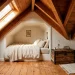 Cozy rustic farmhouse attic bedroom featuring natural wood ceiling beams, wide plank floors, and a built-in bed under slanted eaves.