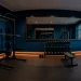 Wide view of a dark home gym painted in moody navy blue with a matte black squat rack and warm LED lighting.