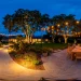 Sprawling modern backyard at twilight featuring layered outdoor lighting, bistro strings, and brass path lights.