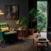 Emerald green mid century accent chair in a moody modern living room with dark charcoal walls and brass lighting.