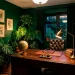 A wide view of a moody dark home office filled with lush indoor plants, vintage desk, and green walls