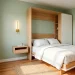 Modern small guest room featuring a space-saving Murphy bed, floating nightstand, and elegant brass wall sconces.