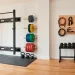 Organized small home gym featuring a wall-mounted folding squat rack and tidy weight plate storage pegs.