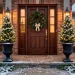 Beautiful classic winter front porch decorated with cedar topiaries and warm lanterns