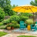 Wide view of a small backyard patio decorated with bright yellow and teal furniture and an outdoor umbrella