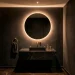 A dramatic and modern tiny powder room featuring dark charcoal walls, a backlit mirror, and a floating marble vanity.
